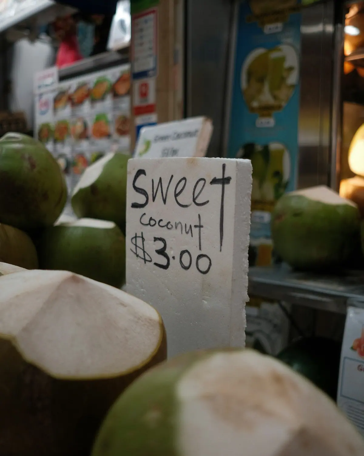 Fresh coconuts at a stall with a hand-written sign: sweet coconut, $3.00