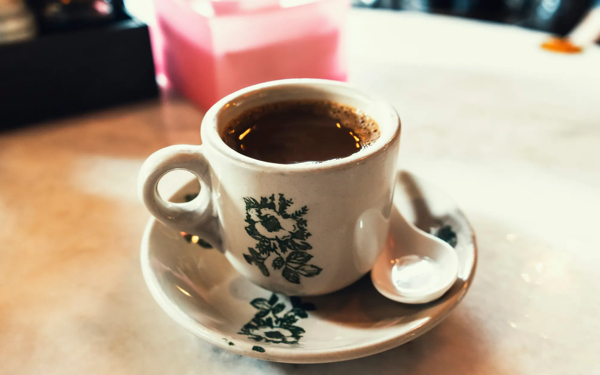 A cup of black kopi in a floral kopitiam cup on a marble table